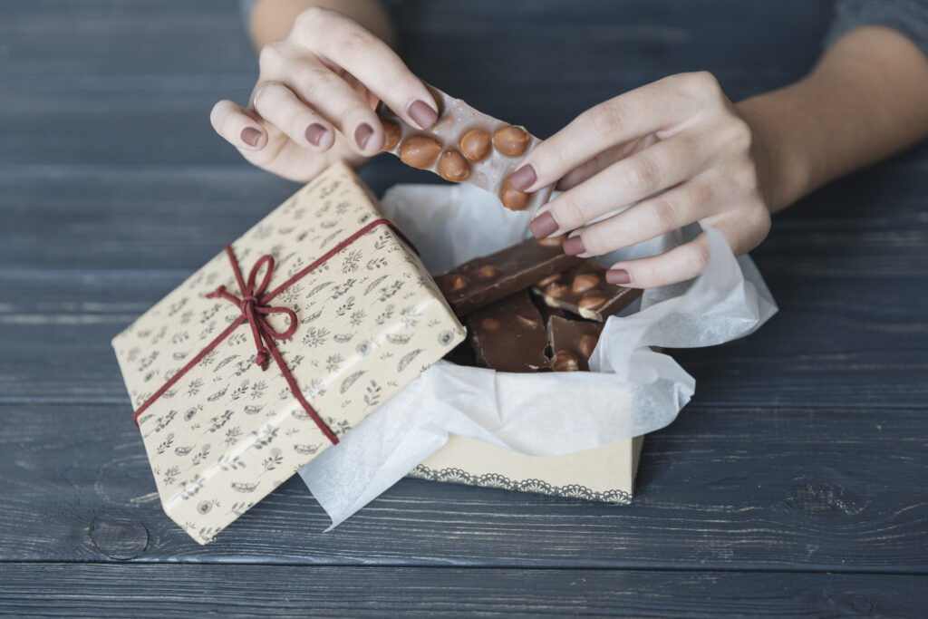 scatola regalo con cioccolato alle nocciole e due mani che lo spezzano