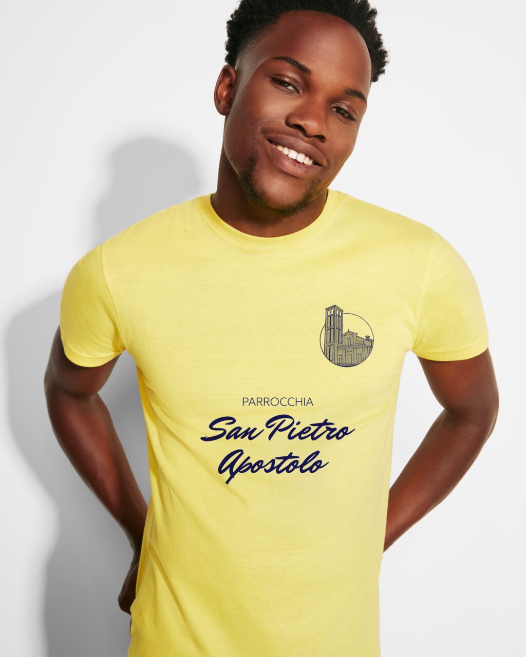 Ragazzo che indossa una maglietta giallo canarino con stampata la scritta Parrocchia San Pietro Apostolo