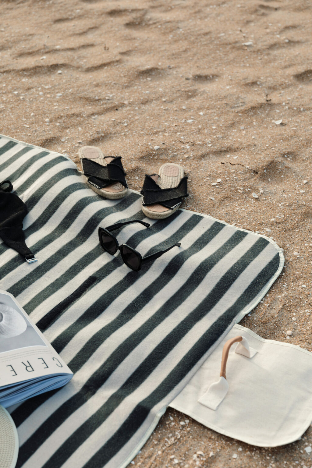 Telo da pic-nic a righe bianche e nere steso sulla sabbia con ciabatte e occhiali da sole appoggiati